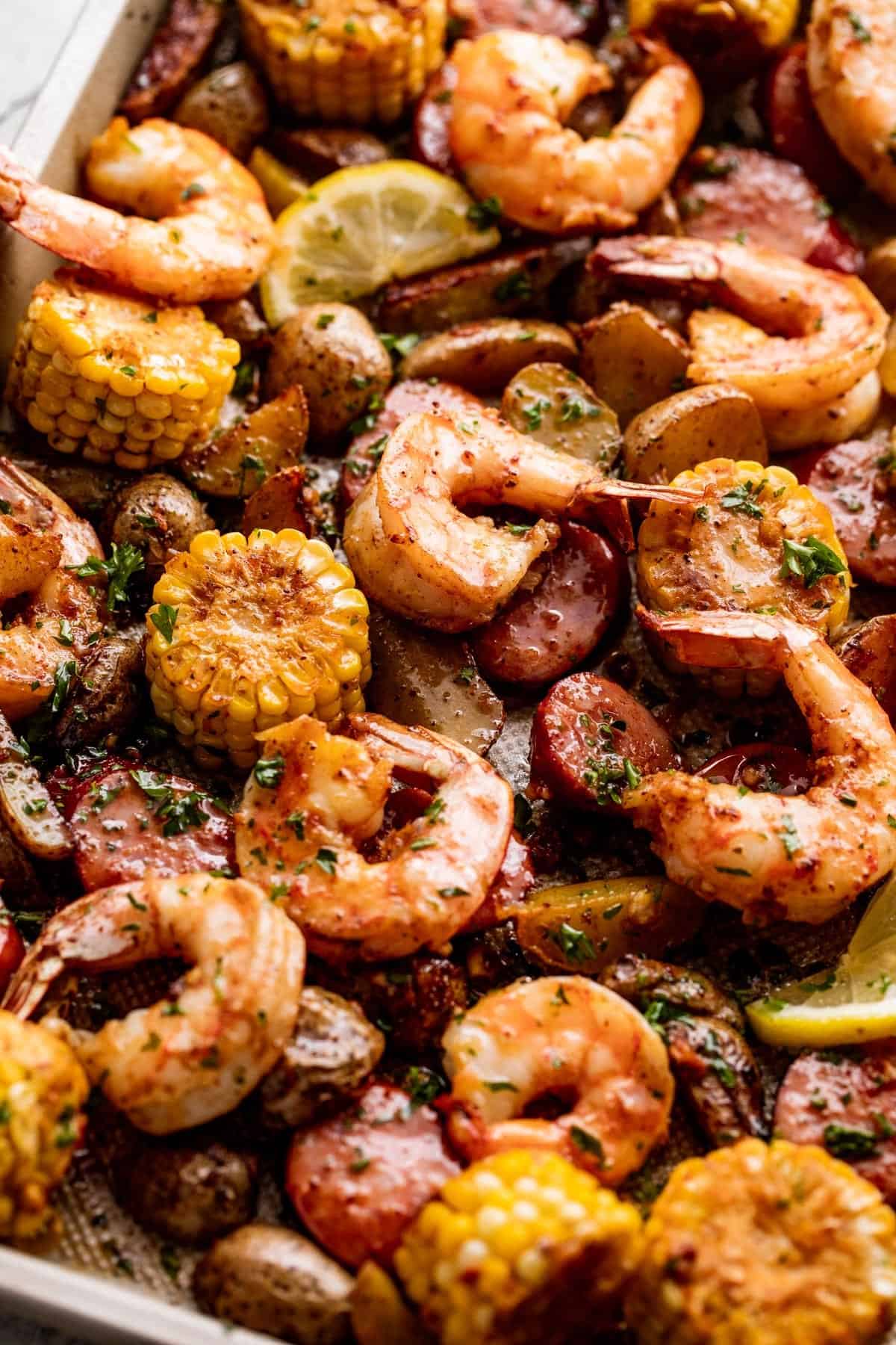 close up shot of baked shrimp, potatoes, sausage, and corn arranged on a sheet pan.