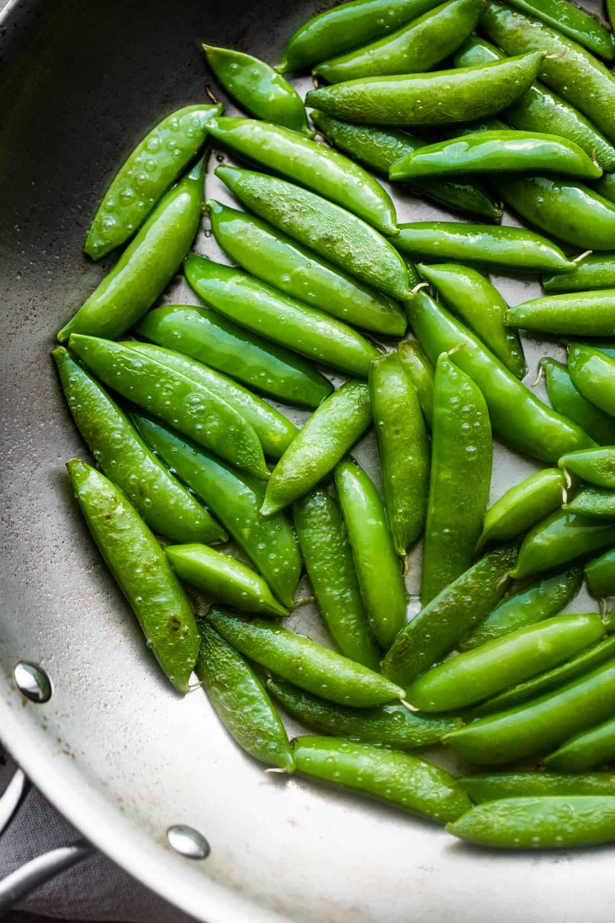 raw fresh sugar snap peas arranged in a silver colored skillet.