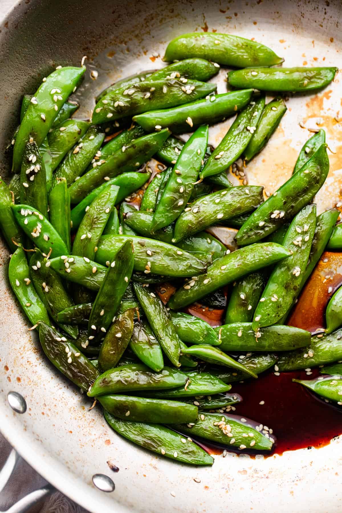 cooked sugar snap peas arranged in a silver colored skillet