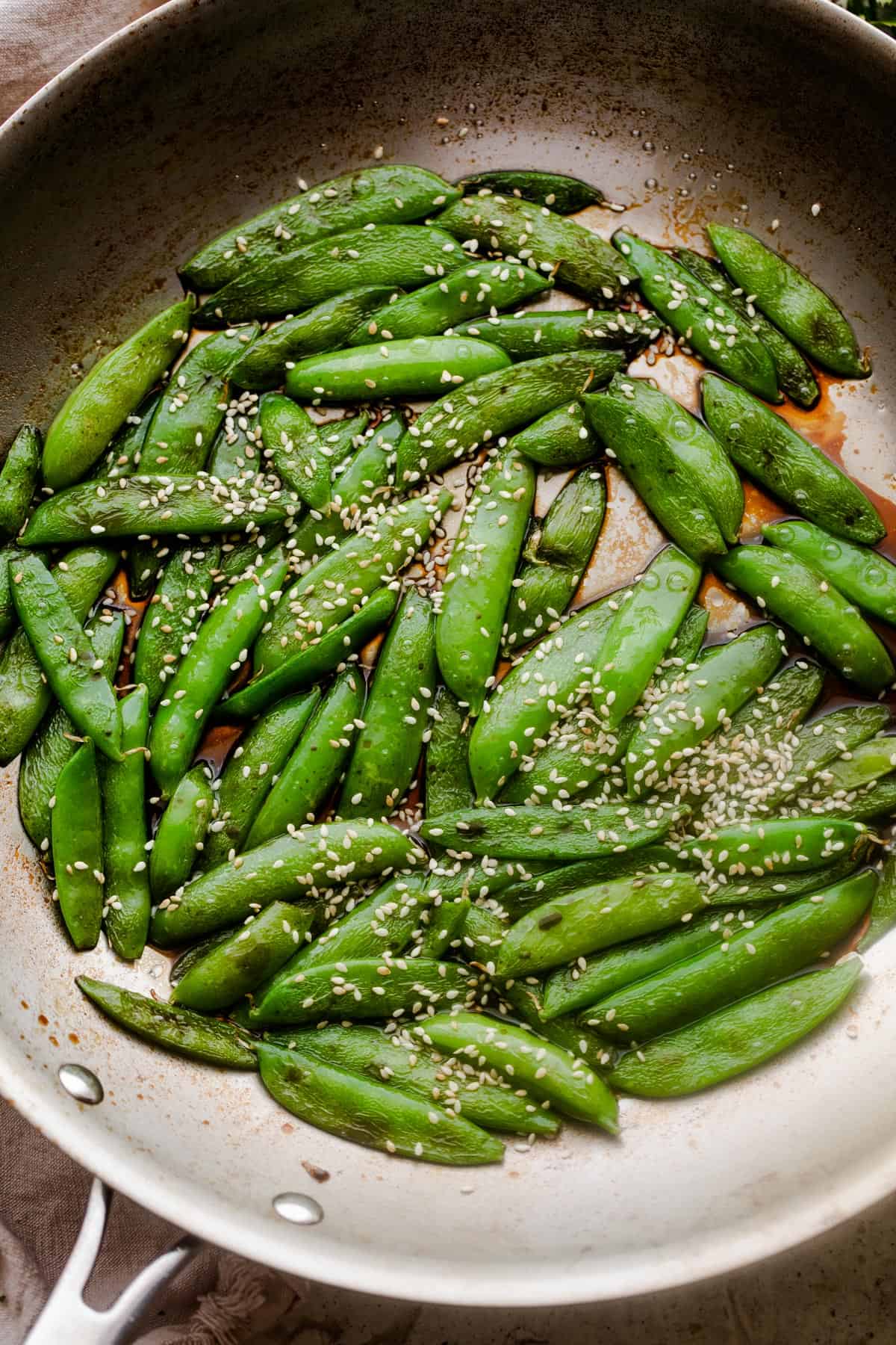 cooked sugar snap peas arranged in a silver colored skillet