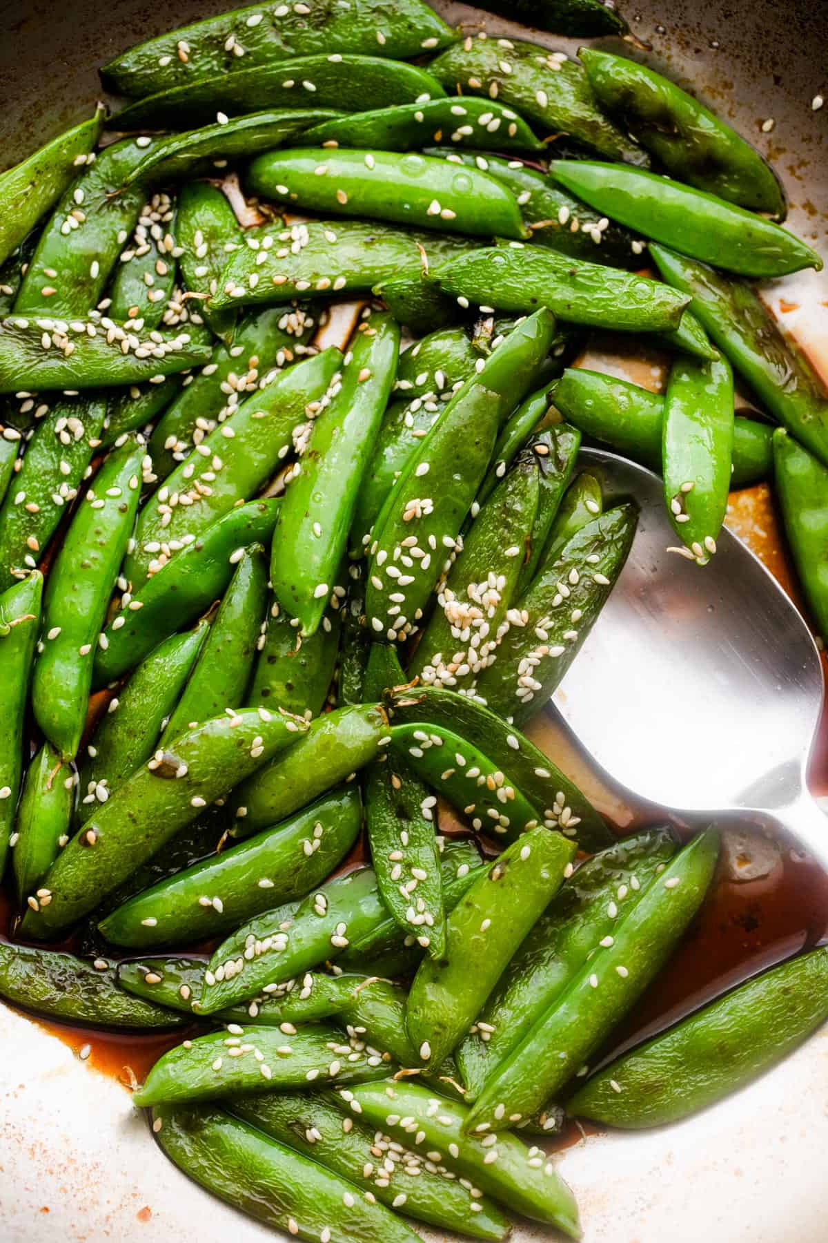 sugar snap peas topped with sesame seeds and a spoon placed nearby.