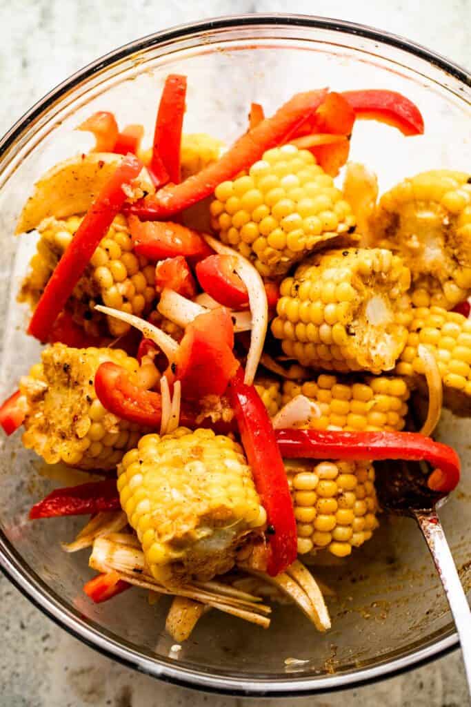 overhead shot of rounds corn on the cob, sliced onions, and sliced red peppers in a glass mixing bowl.