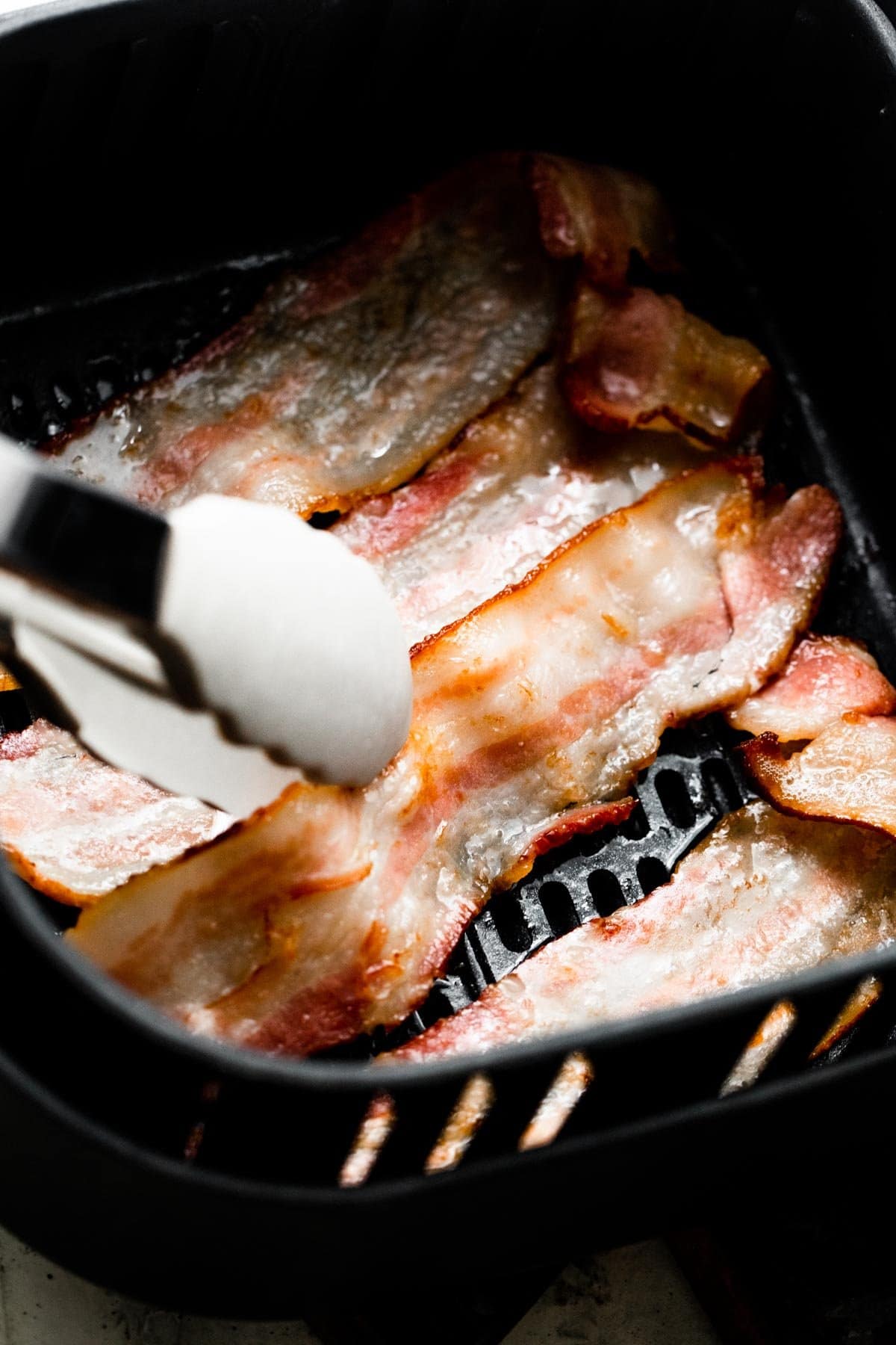 a pair of tongs turning over a slice of bacon.