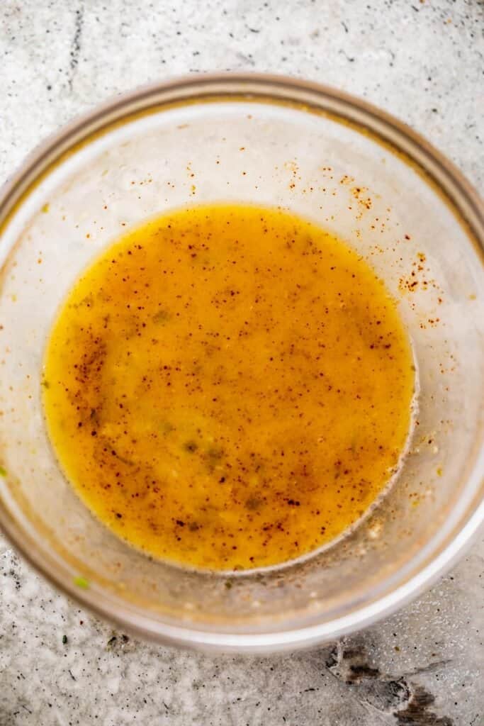 overhead shot of a small glass mixing bowl with melted butter and chili powder mixed inside it.