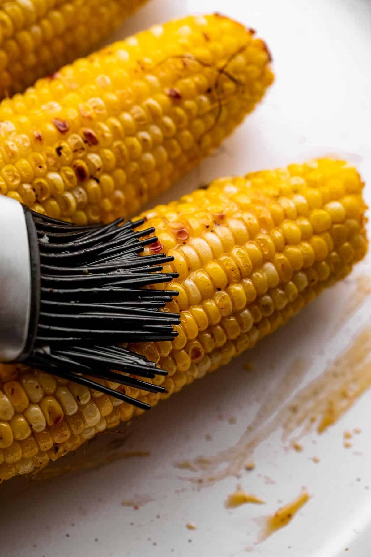 brushing a corn on the cob with butter sauce.
