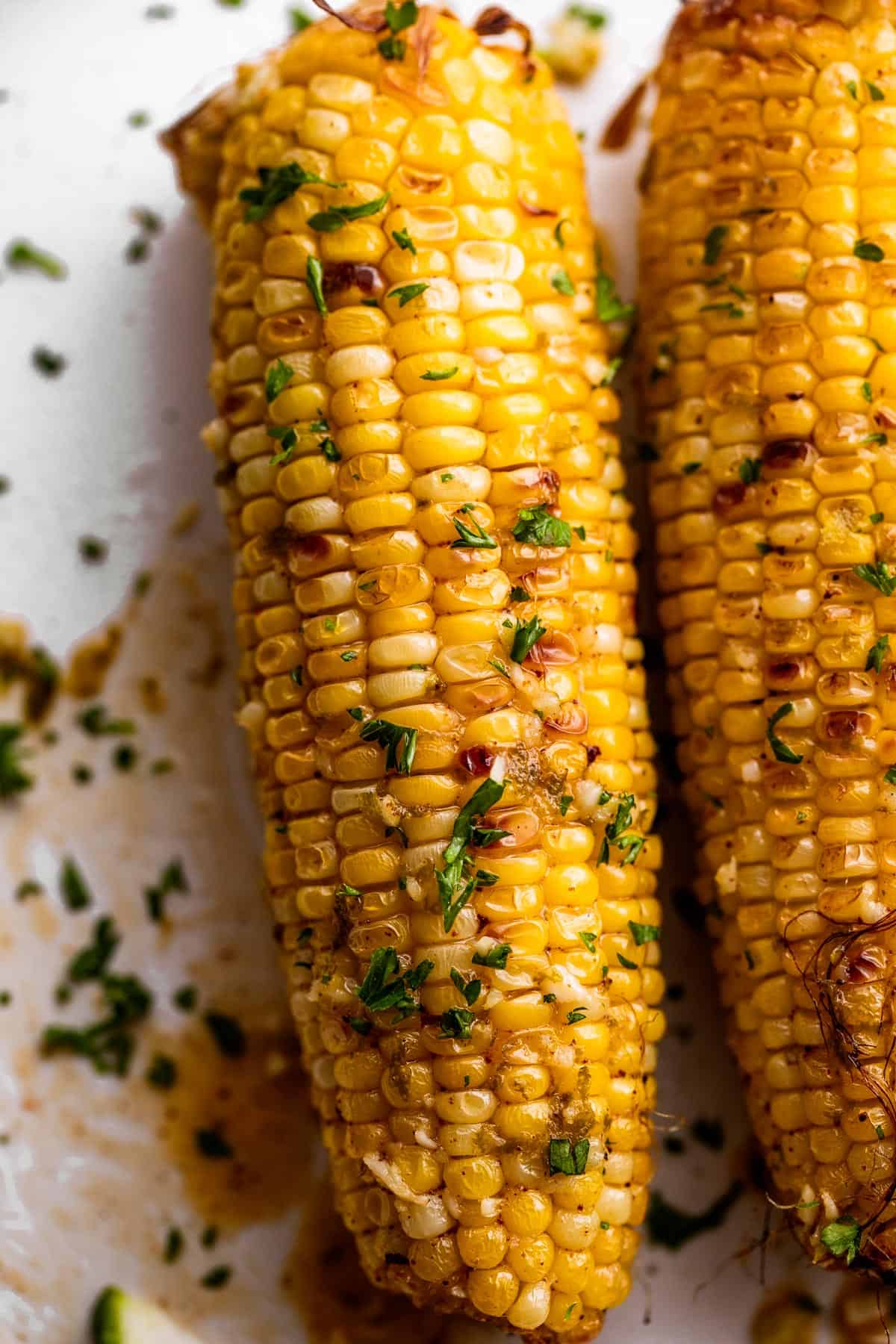 Up close shot of corn on the cob sprinkled with chopped green herbs.