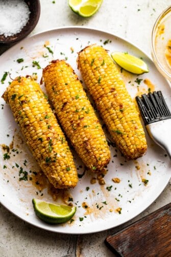 three ears of air fried corn on the cob arranged on a white serving plate.
