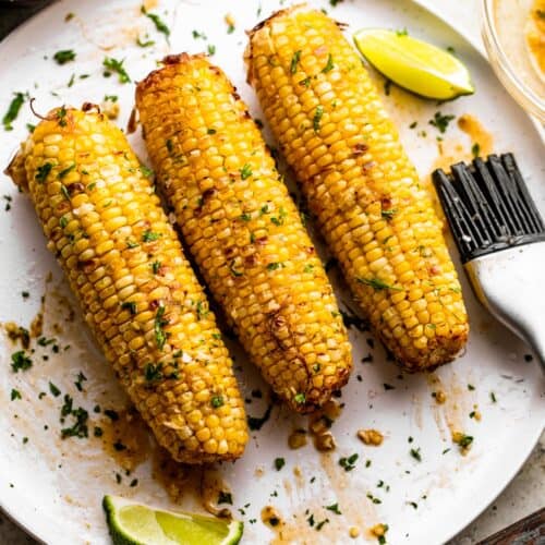 three ears of air fried corn on the cob arranged on a white serving plate.