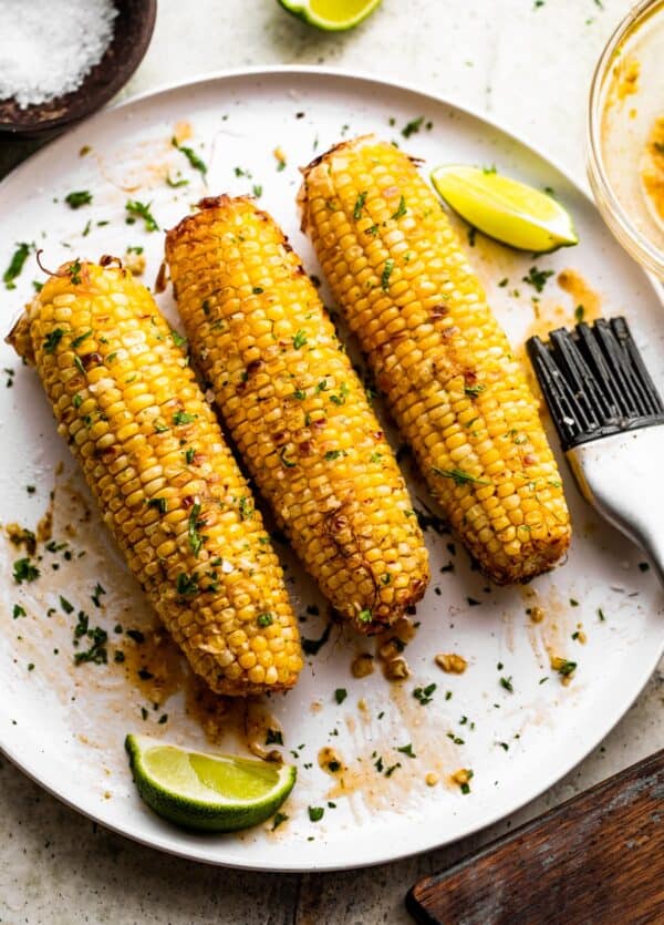 three ears of air fried corn on the cob arranged on a white serving plate.