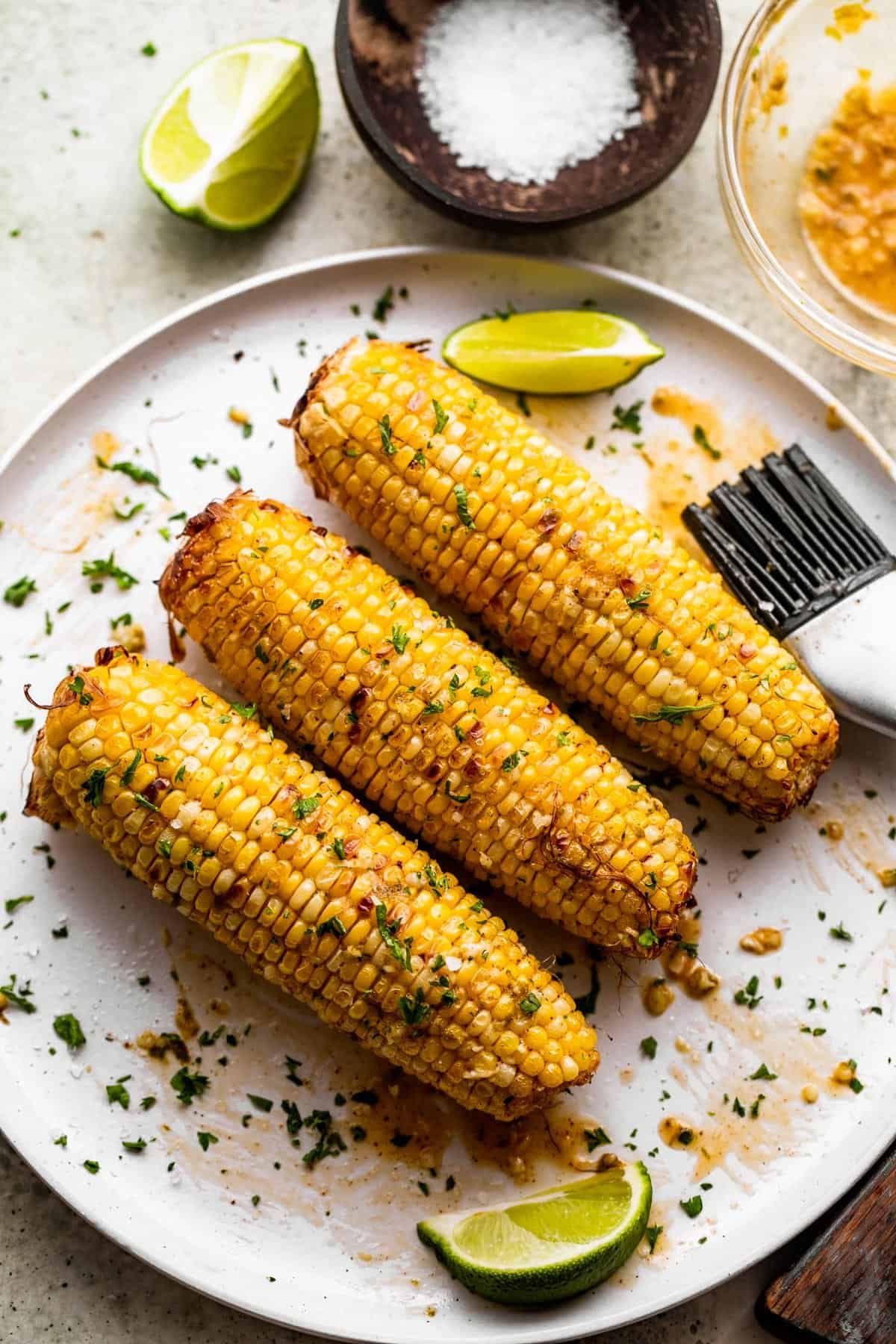 three ears of air fried corn on the cob arranged on a white serving plate.