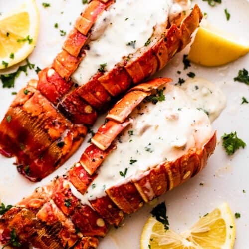two air fryer cooked lobsters arranged on a dinner plate and topped with cream sauce.