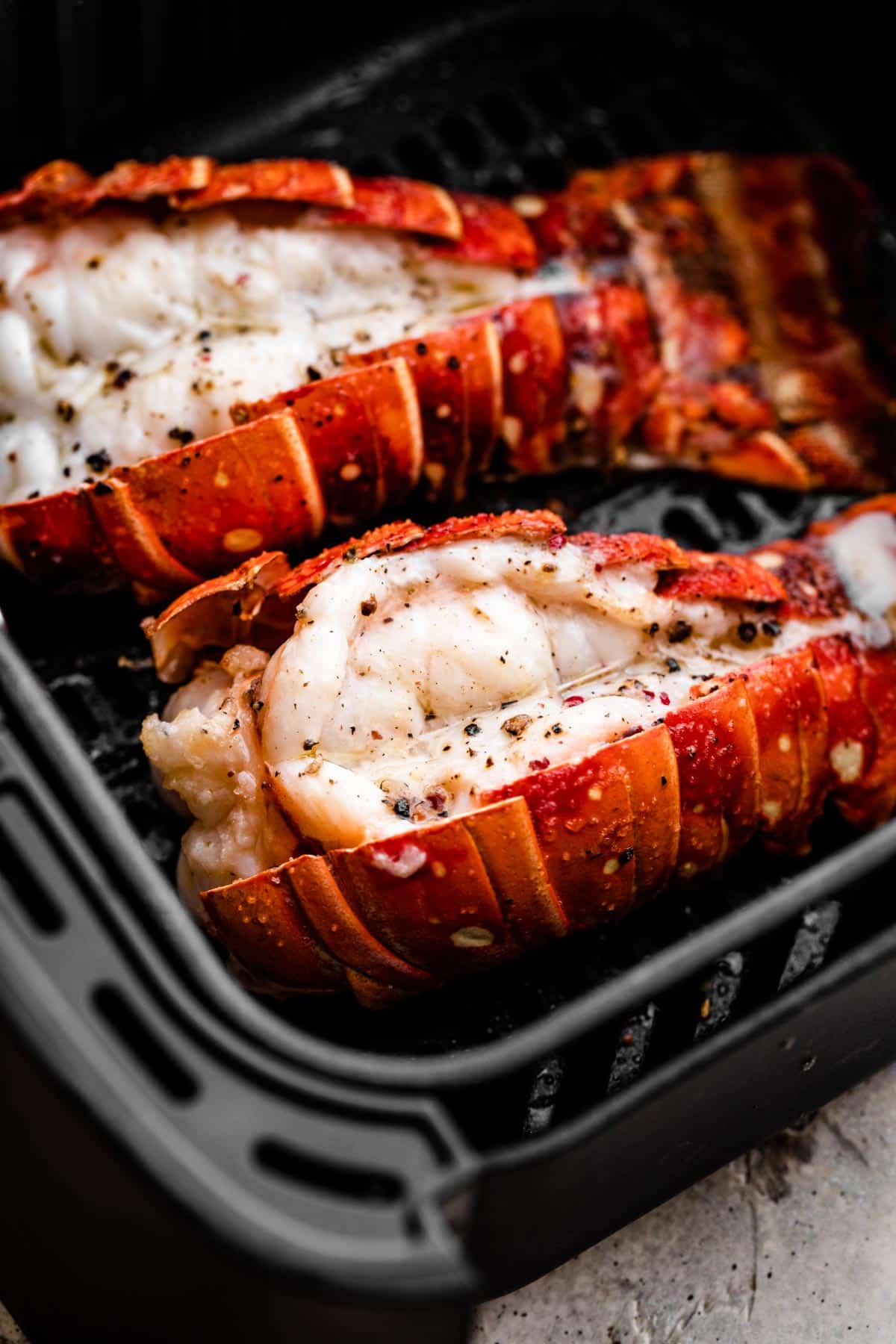 two cooked lobsters in a black air fryer basket.