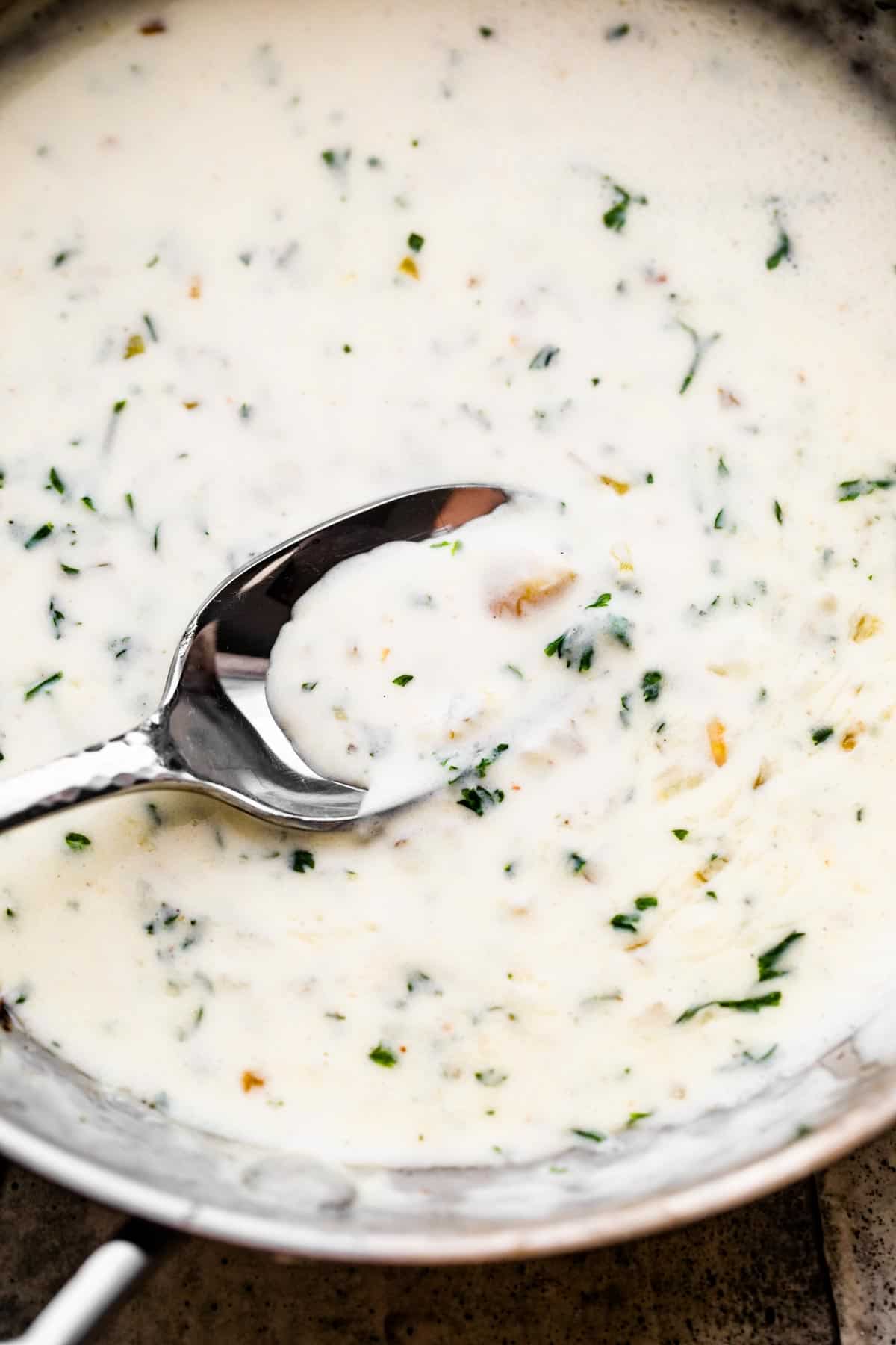 cooking cream sauce in a skillet and stirring through with a large stainless steel spoon.