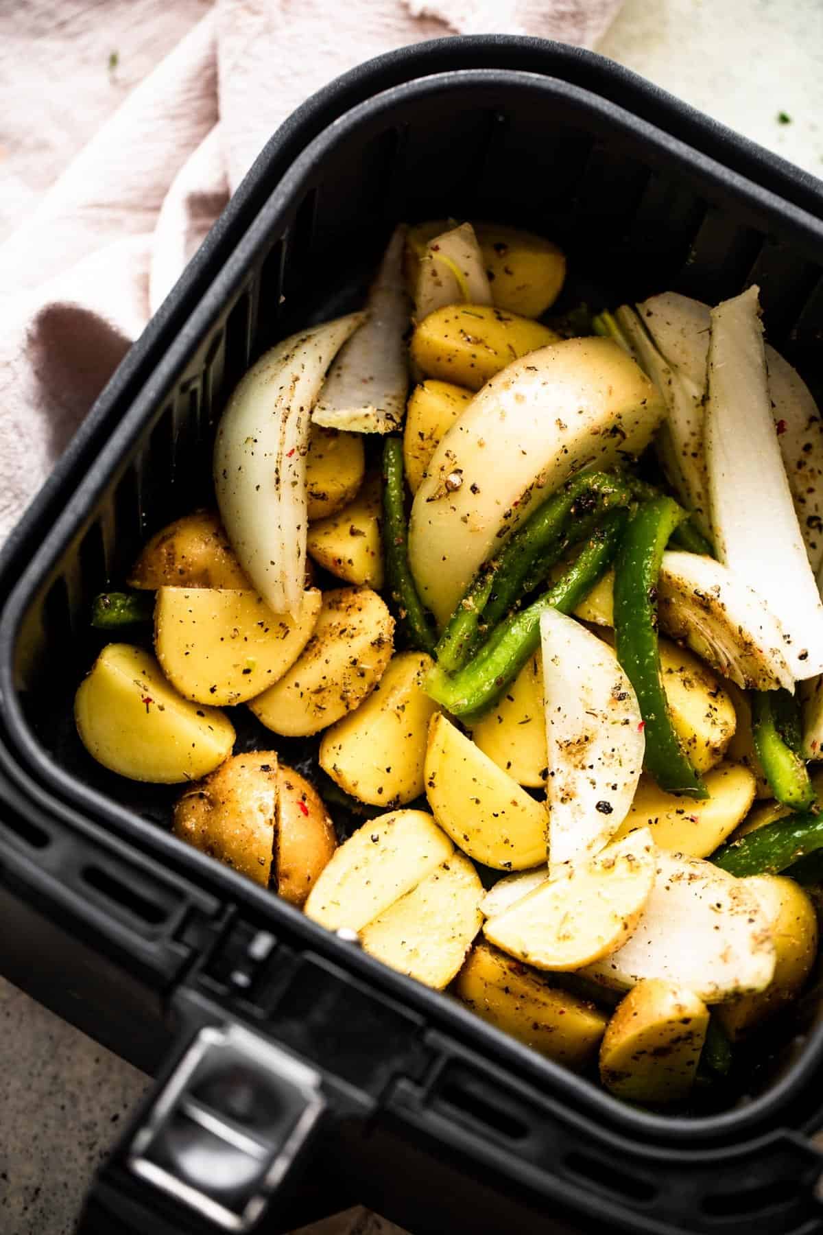 cut up baby potatoes, peppers, and sliced onions arranged in an air fryer basket