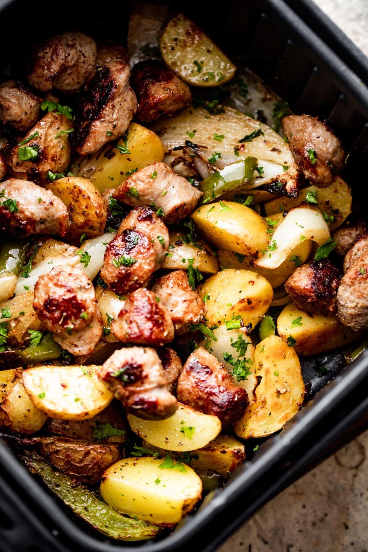 rounds of sausage, cut up baby potatoes, peppers, and sliced onions arranged in an air fryer basket