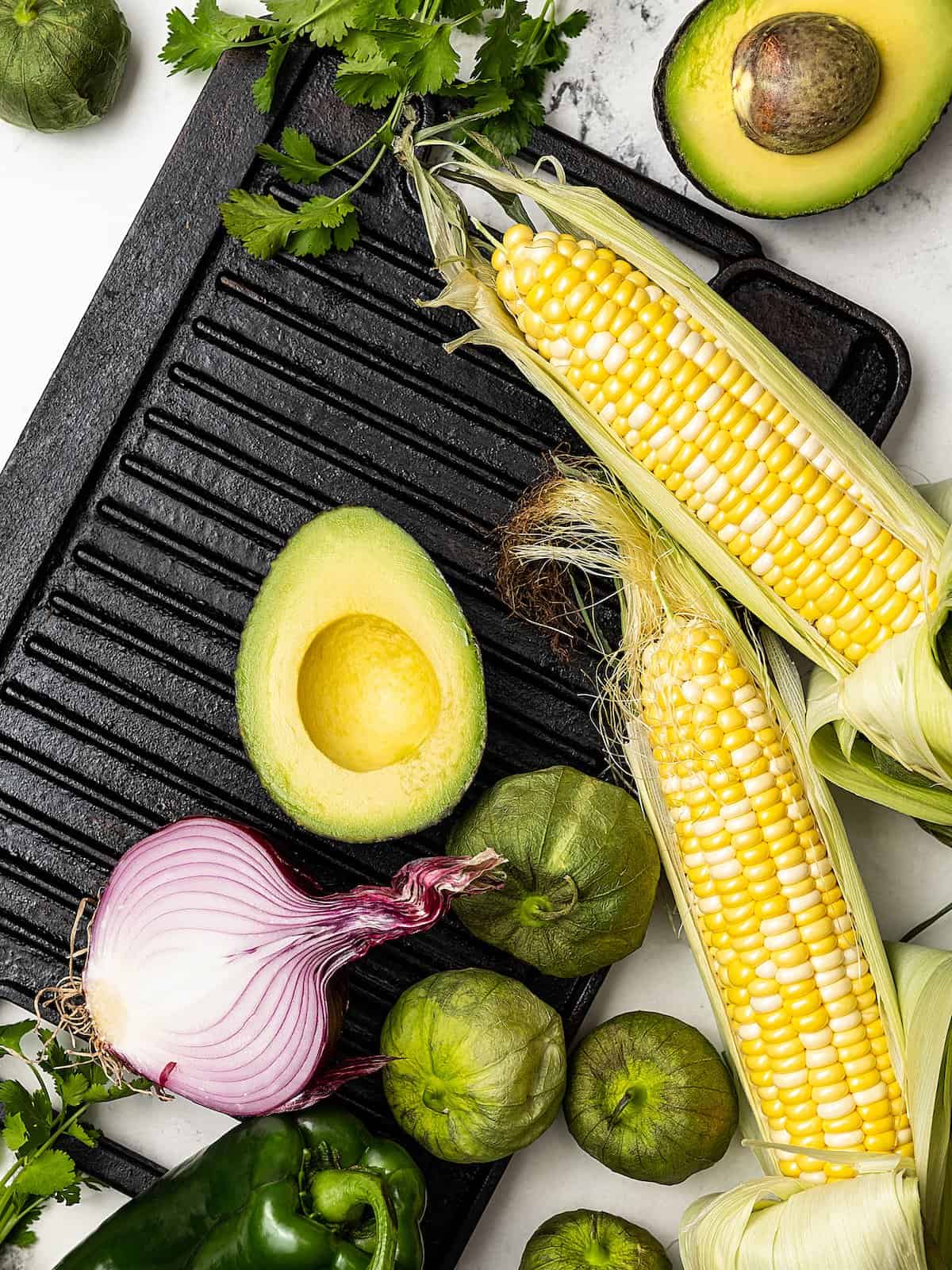 Fresh corn, avocado, red onion, cilantro and tomatillos on top of a stovetop grill pan