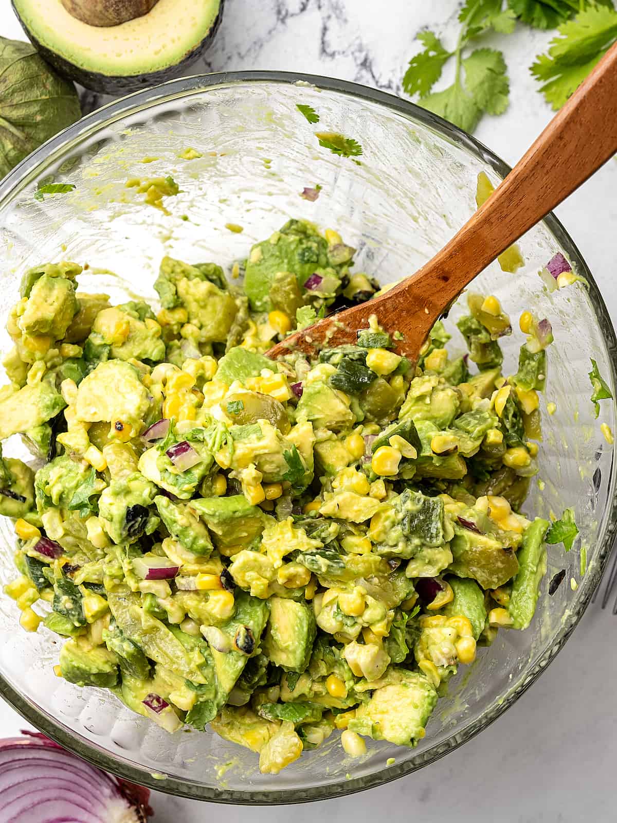 Grilled corn being mixed with avocado chunks, chopped tomatillos, green chile, red onion, cilantro and salt