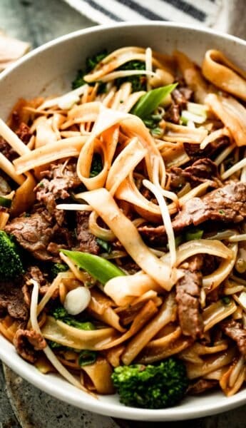 up close overhead shot of a white bowl with beef chow fun and two chopsticks resting on the left side of the bowl.