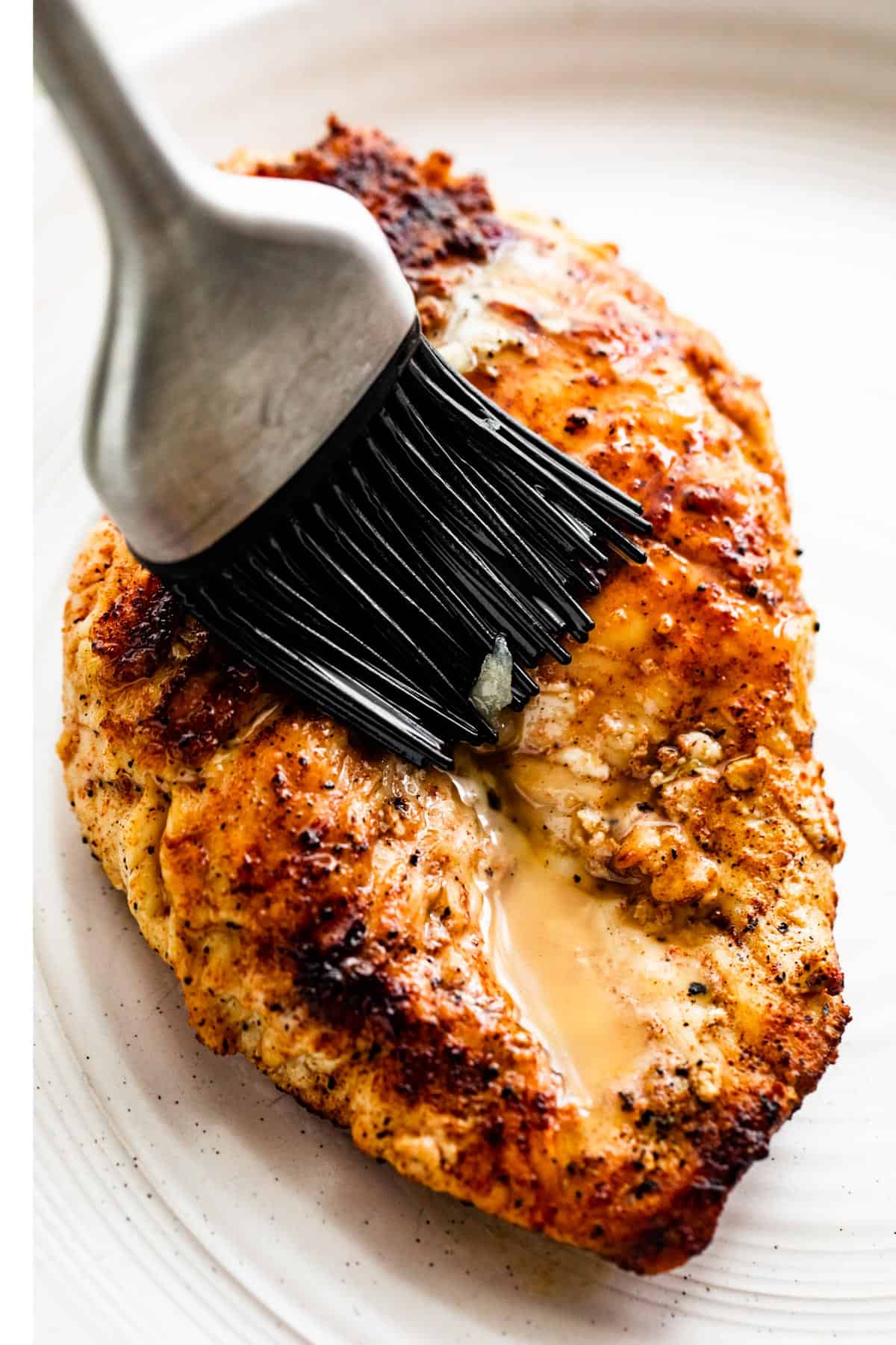 pastry brush brushing garlic butter over a grilled chicken breast.