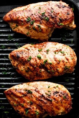 three grilled blackened chicken breasts arranged on a grill in a single row.
