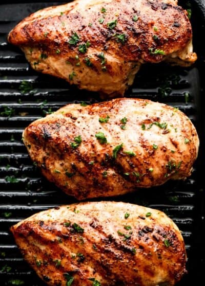 three grilled blackened chicken breasts arranged on a grill in a single row.
