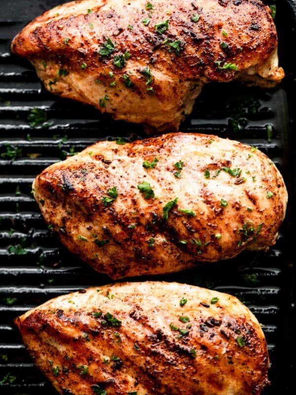 three grilled blackened chicken breasts arranged on a grill in a single row.