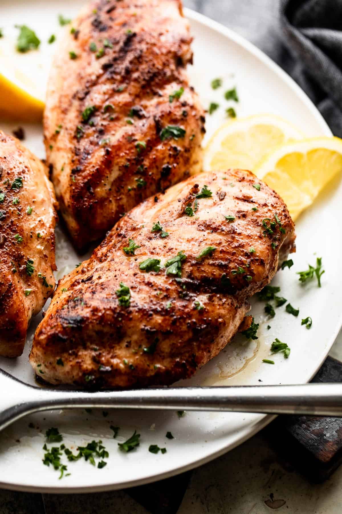 three pieces of grilled blackened chicken arranged on a white plate with lemon wedges to the side and a pastry brush set at the bottom of the plate.