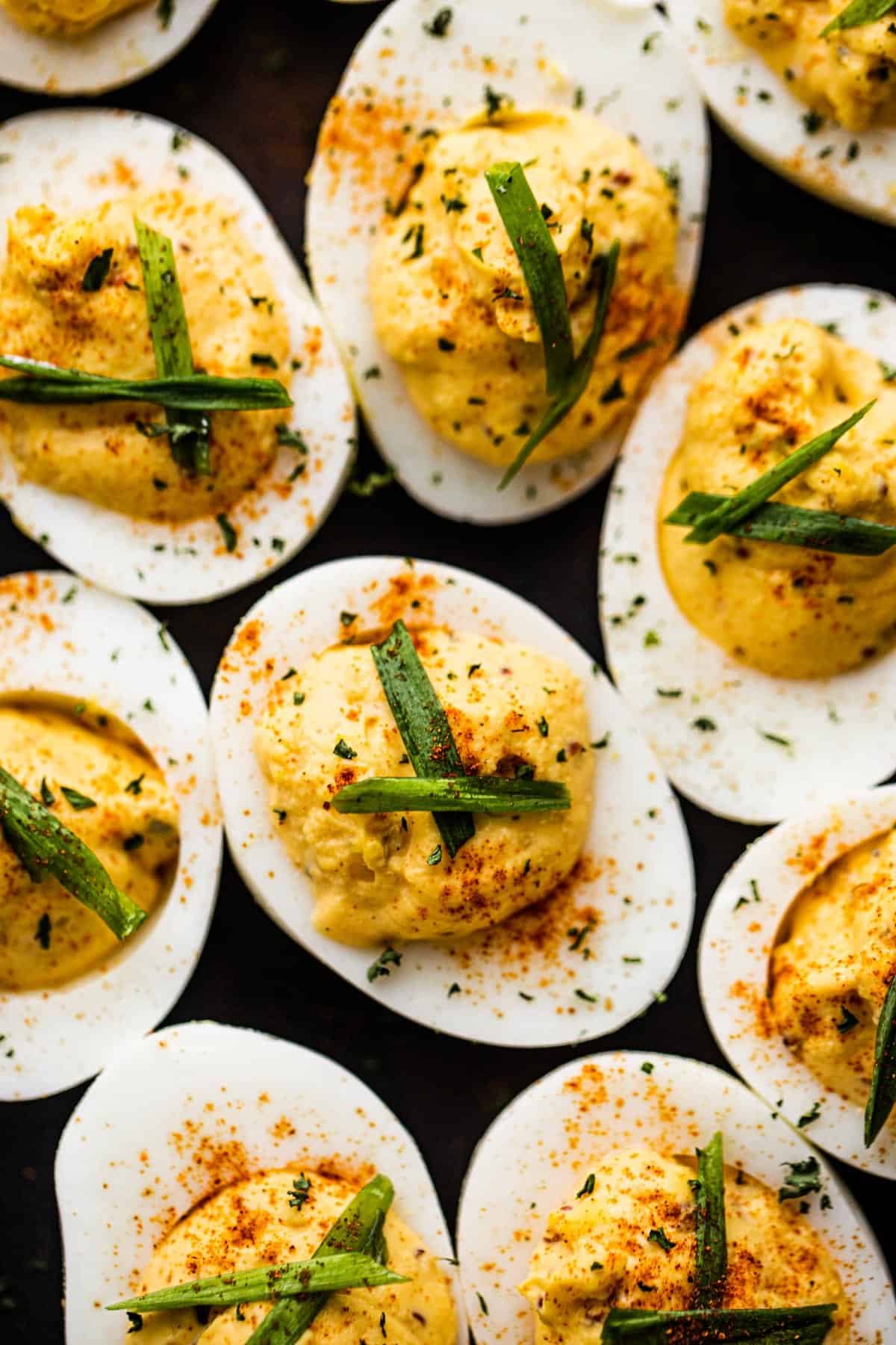 Overhead shot of deviled eggs garnished with chives and parsley and set on a dark backdrop.