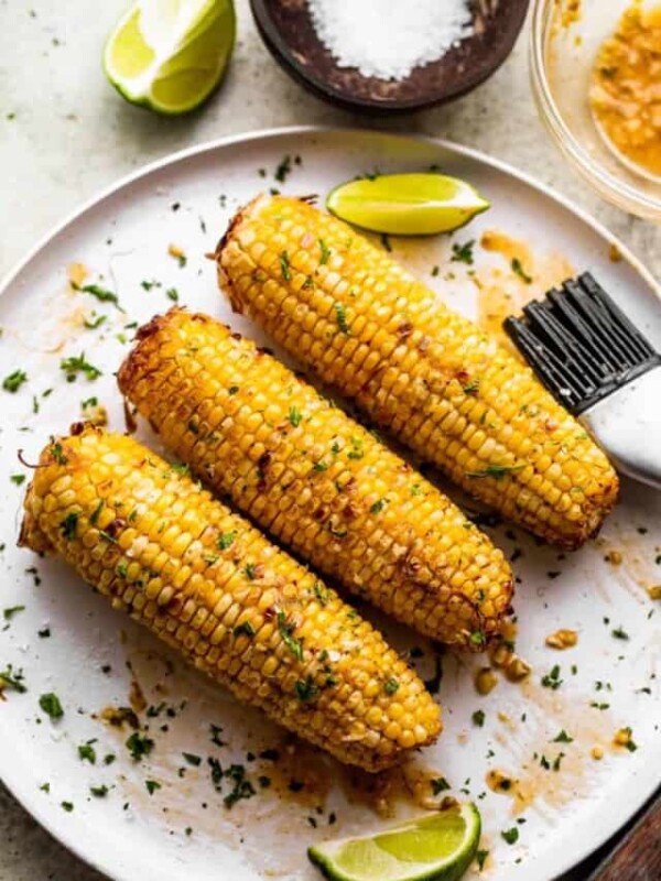 three ears of air fried corn on the cob arranged on a white serving plate.