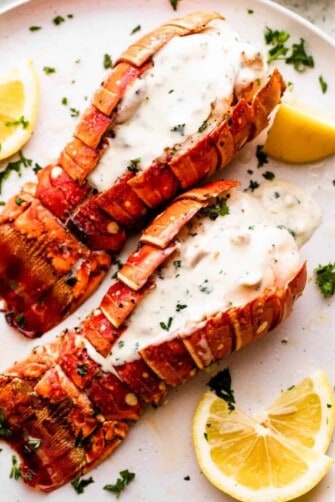 two air fryer cooked lobsters arranged on a dinner plate and topped with cream sauce.