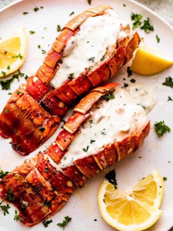 two air fryer cooked lobsters arranged on a dinner plate and topped with cream sauce.