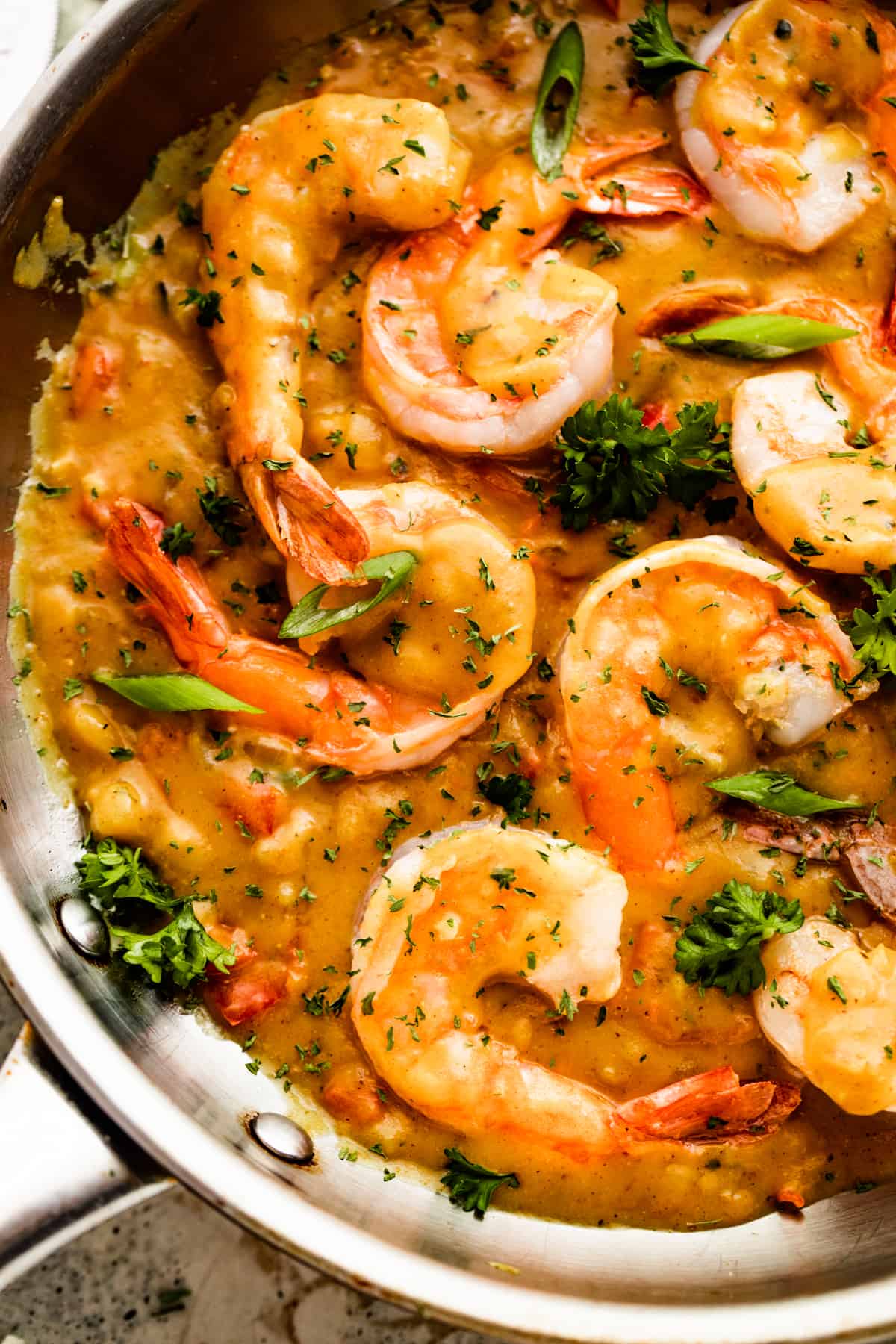 stainless steel skillet with prawns nestled in a curry sauce.
