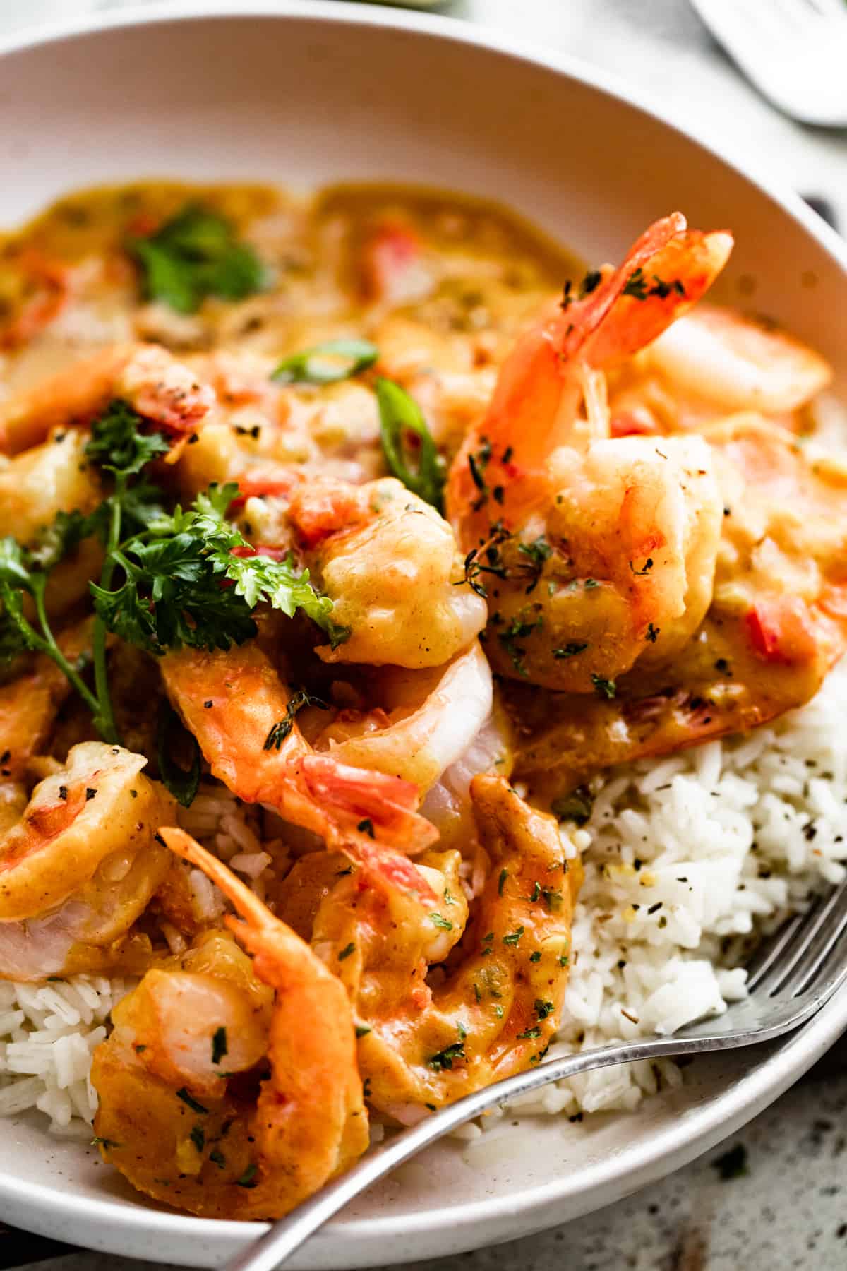 close up shot of a white bowl with shrimp curry served over white rice, with a fork set inside the bowl.