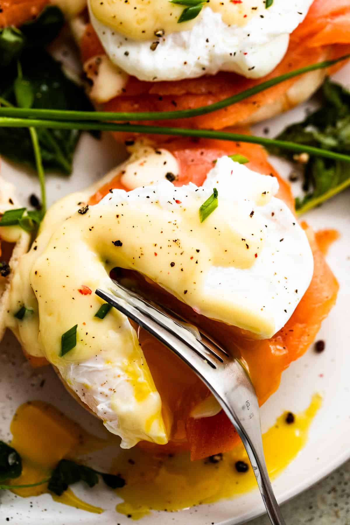 a fork cutting through a poached egg set atop an english muffin and smoked salmon.