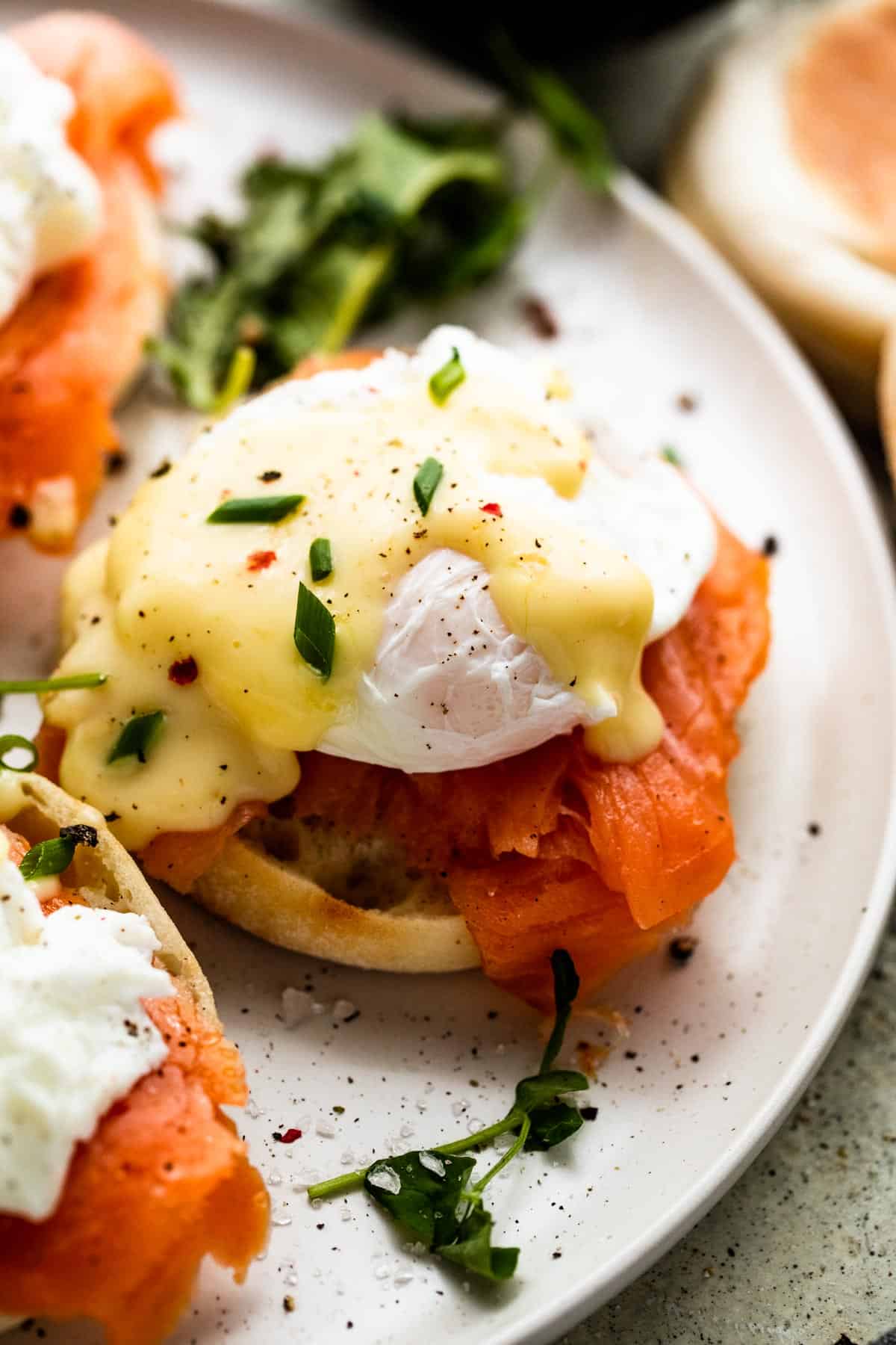 an english muffin topped with a slice of smoked salmon and a poached egg; top is garnished with hollandaise sauce and chopped chives.