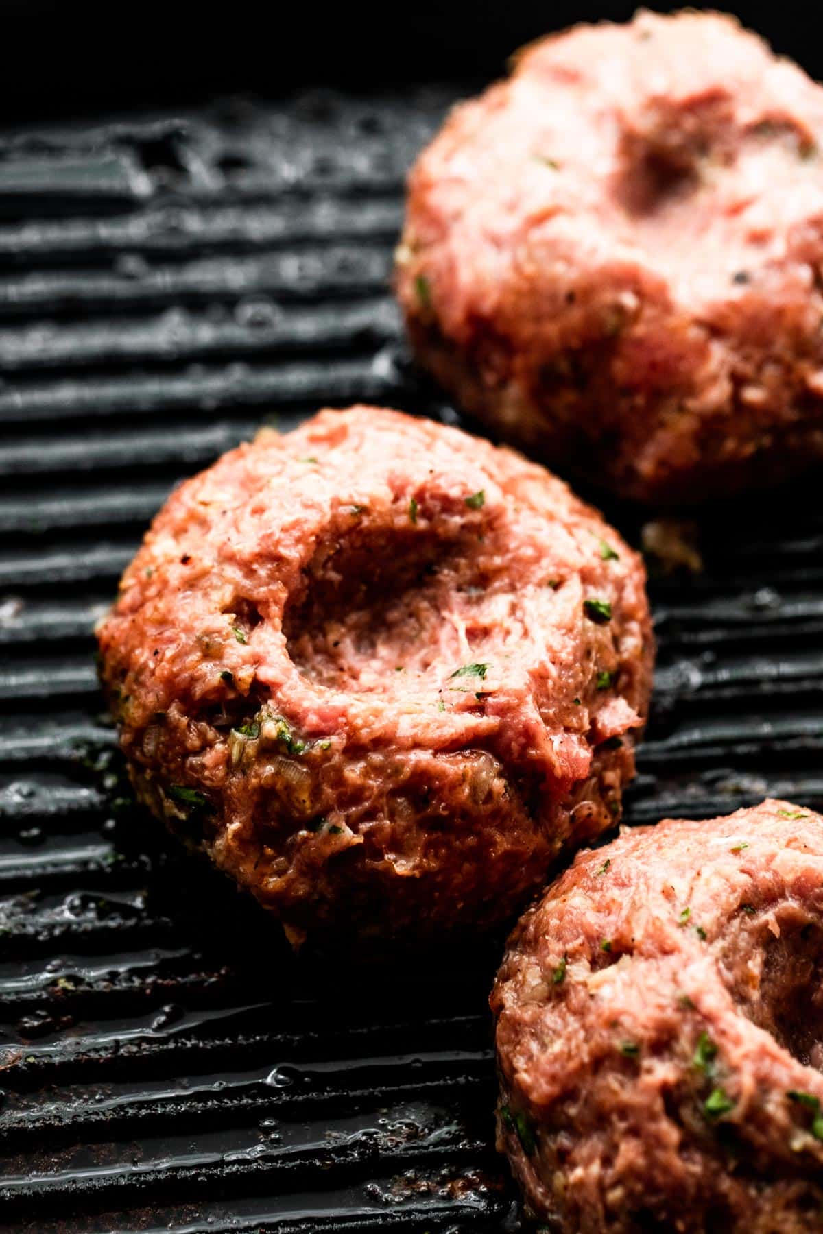 With just a few simple ingredients, these Juicy Grilled Turkey Burgers are guaranteed to turn out savory, tender, and perfect, every time! black grill with three ground turkey patties with thumb indentation in the center of each patty.