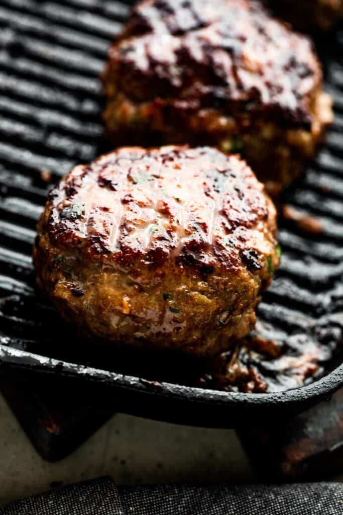 grilling two turkey burgers on a black grill pan.