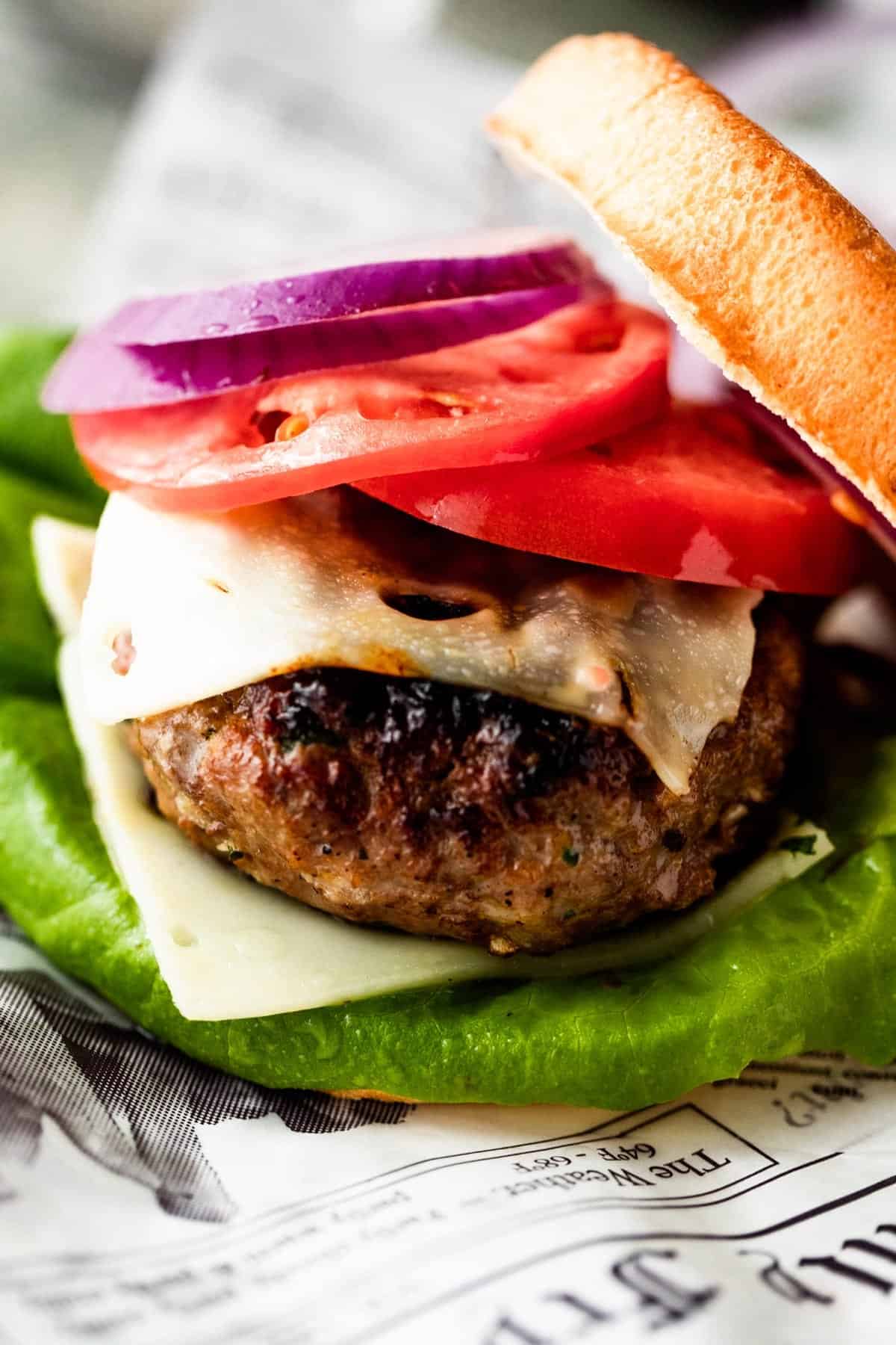 close up shot of a grilled turkey burger dressed with tomato slices, cheese slices, red onion slices, and green salad.