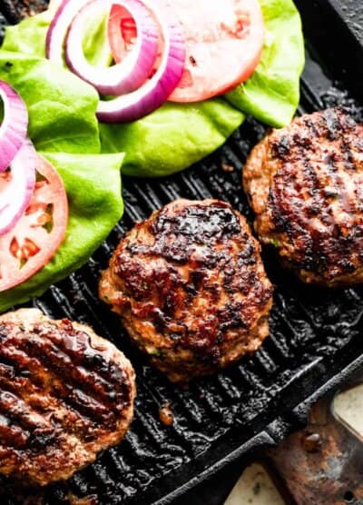 three turkey burgers on a black backdrop with lettuce, tomatoes, and red onion slices arranged alongside the burgers.