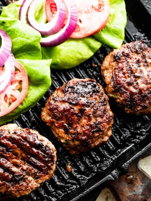 three turkey burgers on a black backdrop with lettuce, tomatoes, and red onion slices arranged alongside the burgers.