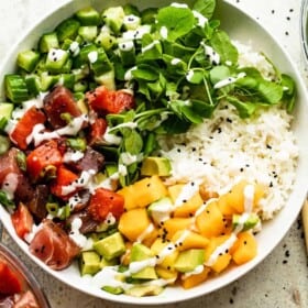 overhead shot of a poke bowl with rice, diced mango, diced tuna, diced salmon, diced cucumbers, diced avocados, and greens.