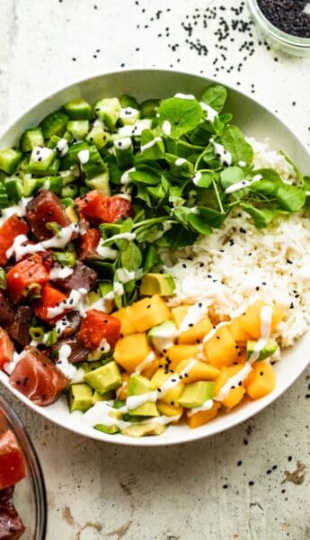 overhead shot of a poke bowl with rice, diced mango, diced tuna, diced salmon, diced cucumbers, diced avocados, and greens.