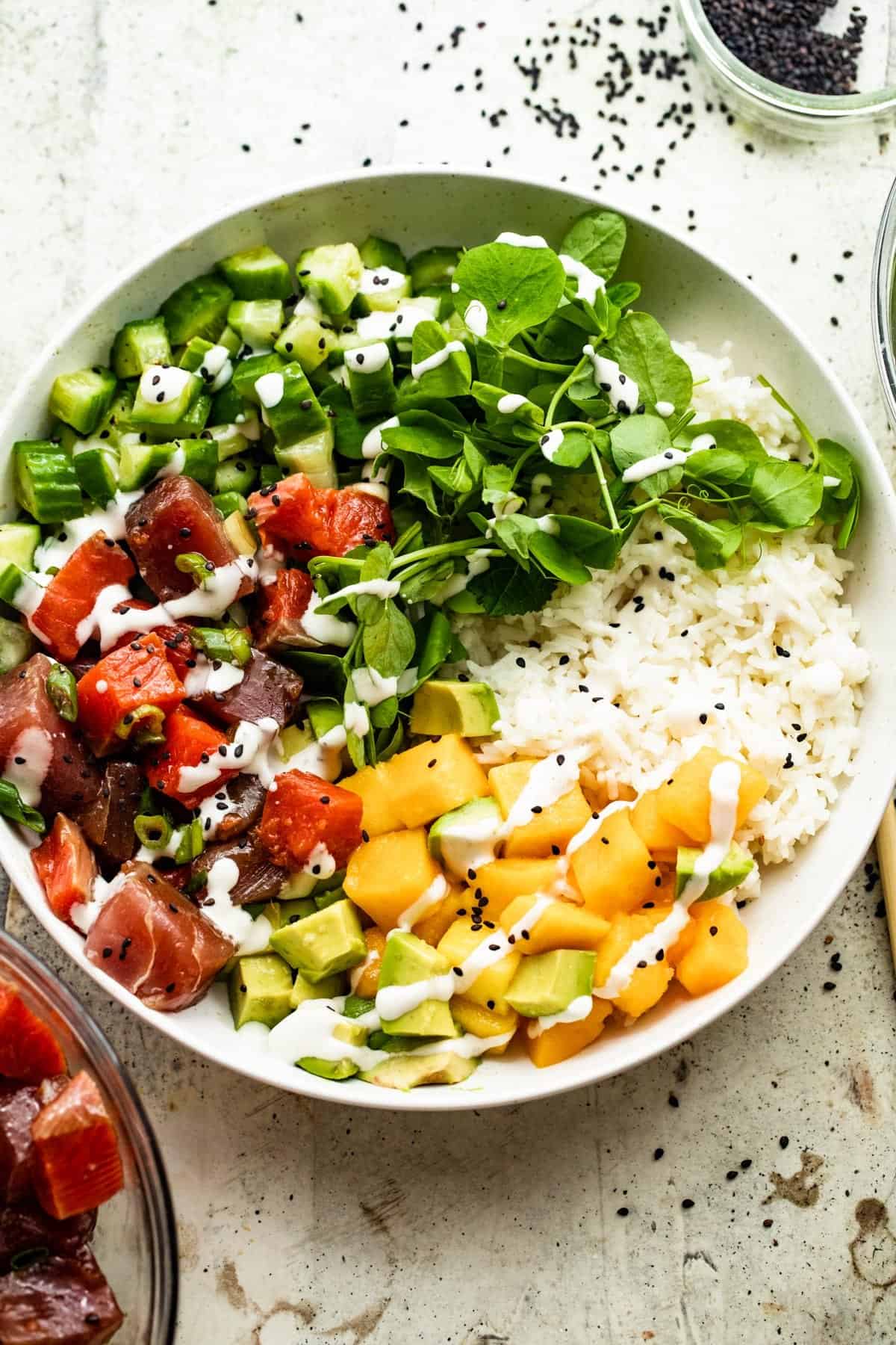 overhead shot of a poke bowl with rice, diced mango, diced tuna, diced salmon, diced cucumbers, diced avocados, and greens.