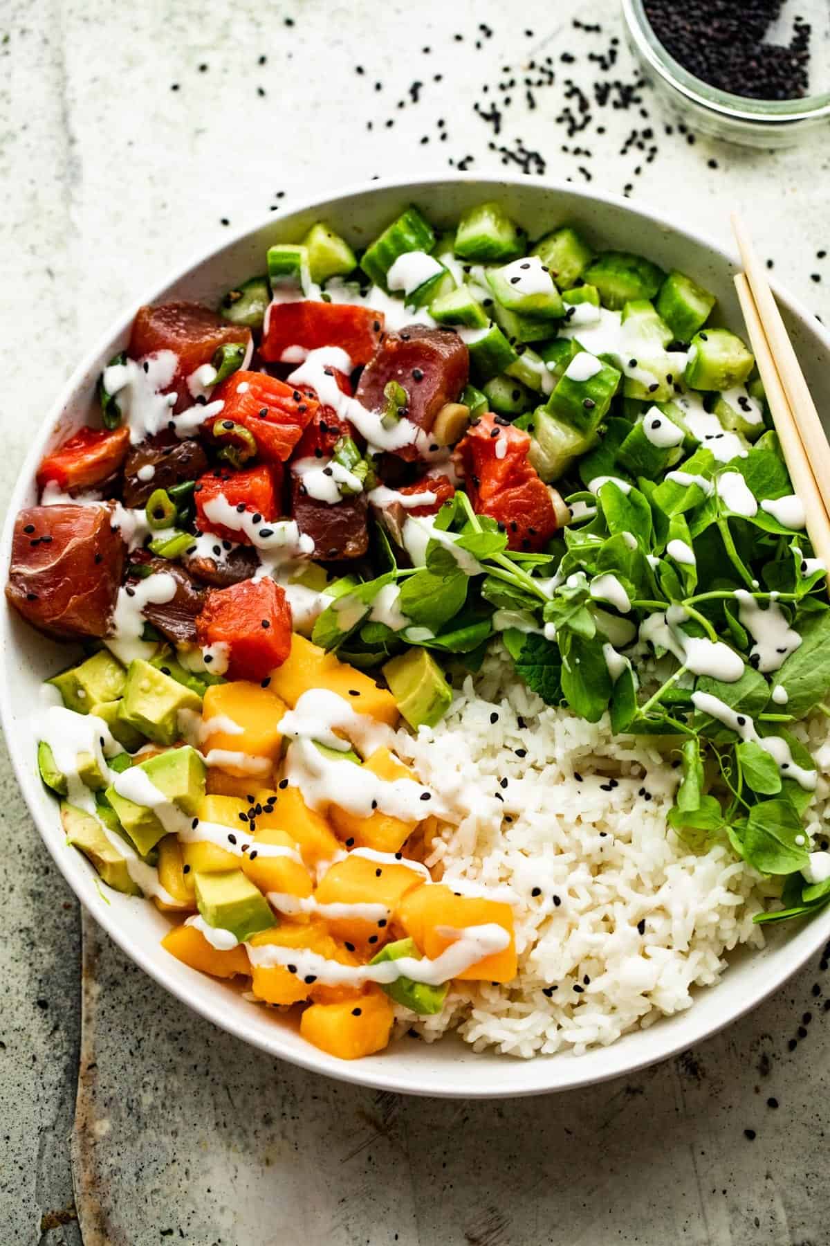 overhead shot of a poke bowl with rice, diced mango, diced tuna, diced salmon, diced cucumbers, diced avocados, and greens.