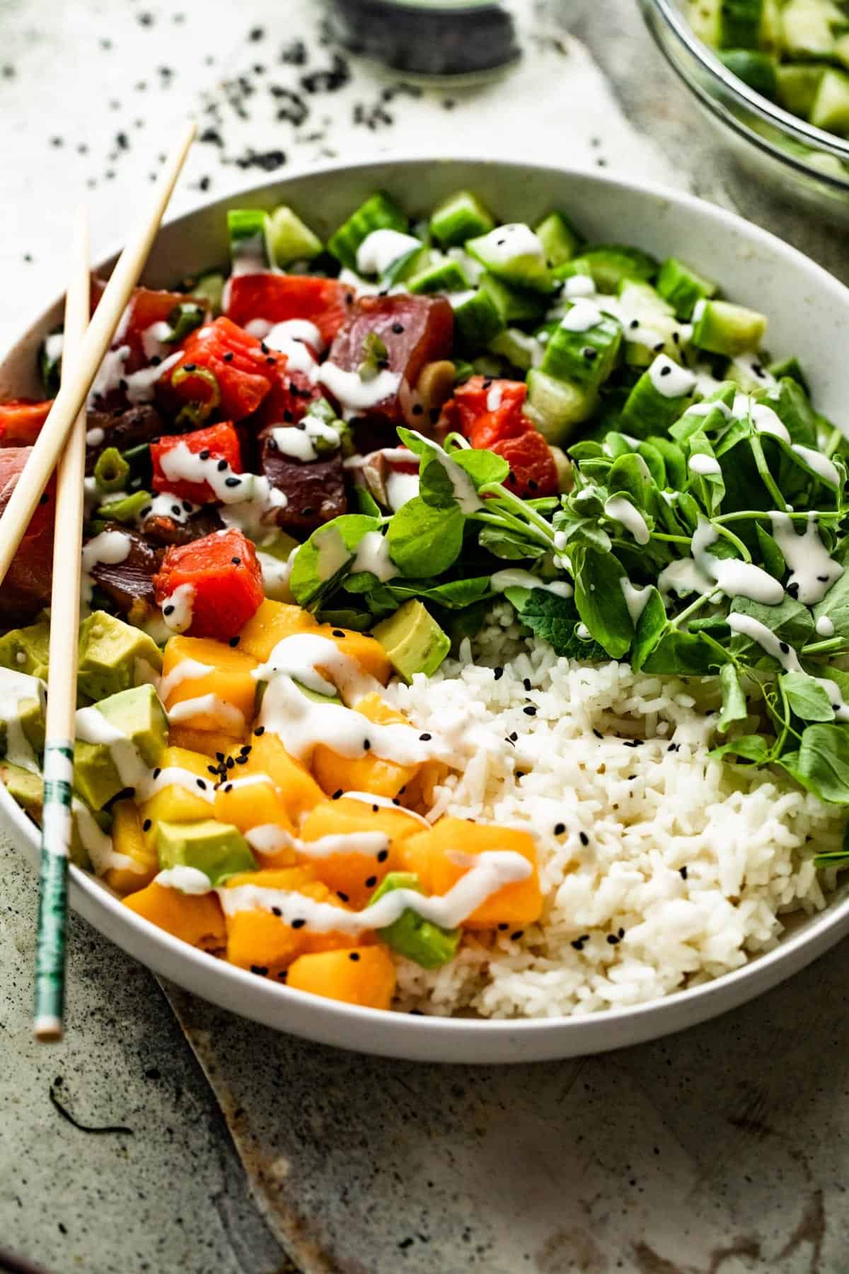 side shot of a poke bowl with rice, diced mango, diced tuna, diced salmon, diced cucumbers, diced avocados, and greens.