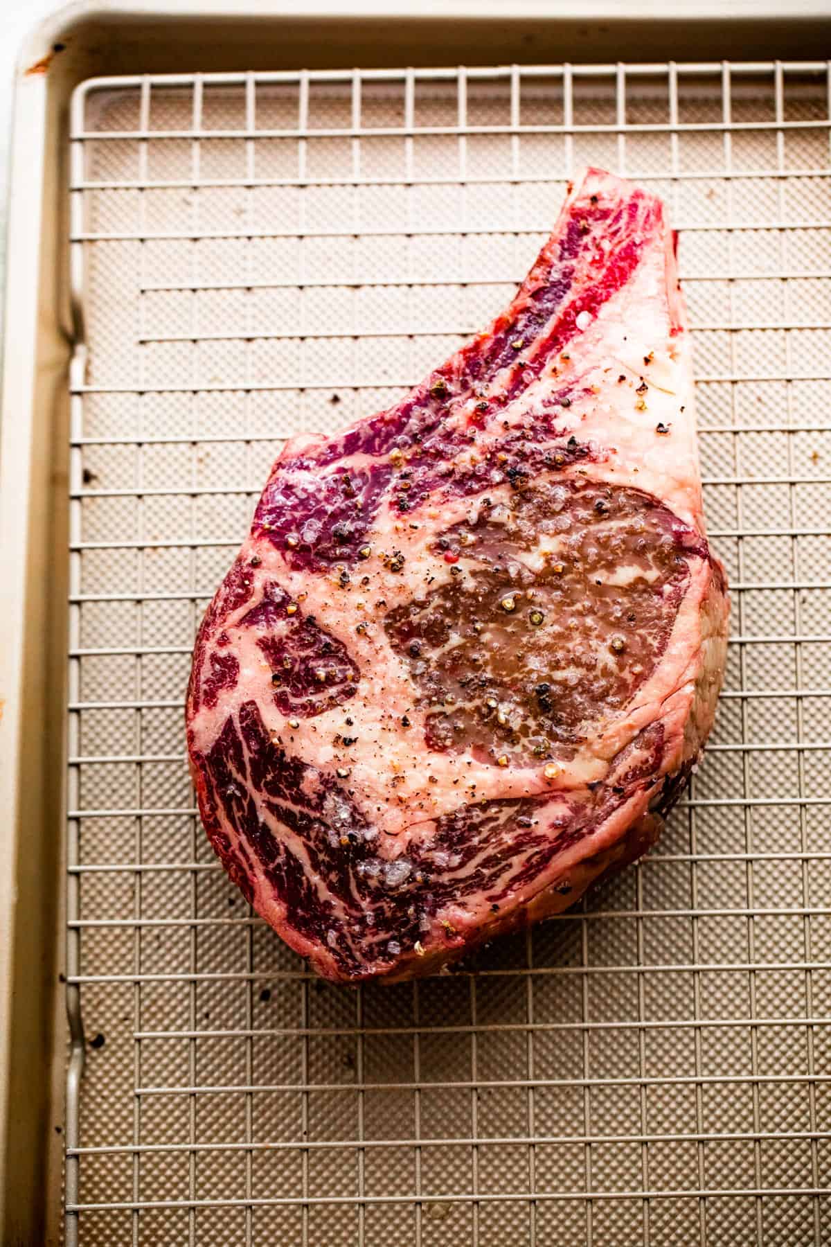 overhead shot of raw ribeye steak placed on a wire rack that's set over a baking sheet.