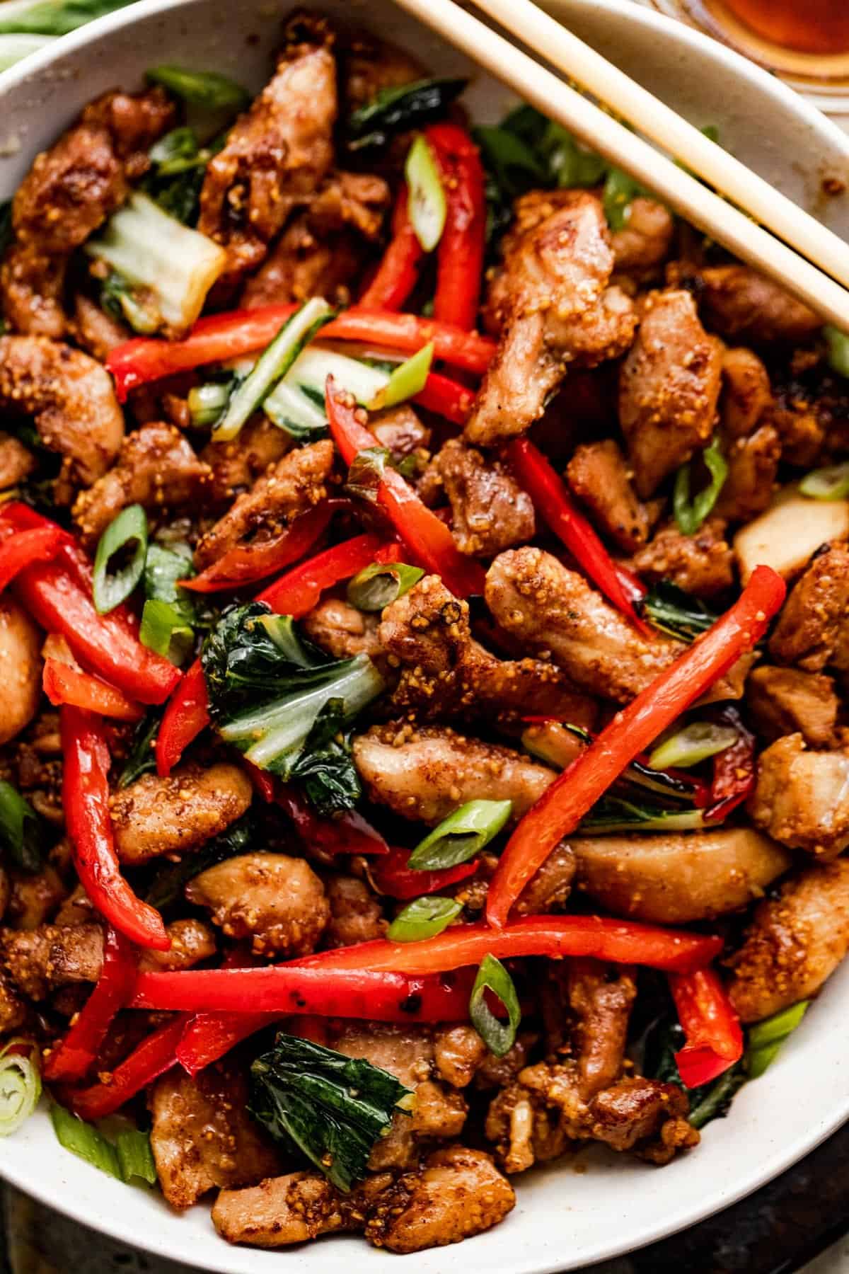 upclose photo of salt and pepper chicken in a white bowl with two chopsticks resting on top of the bowl.