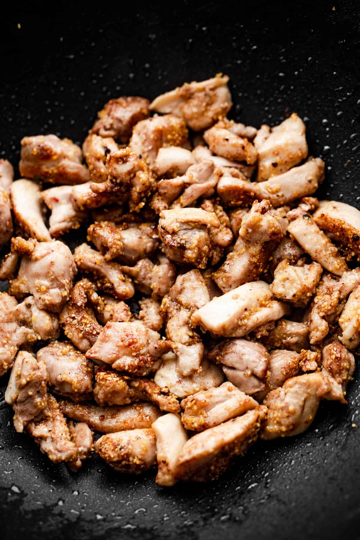 cooking cut up chicken thighs in a black wok.