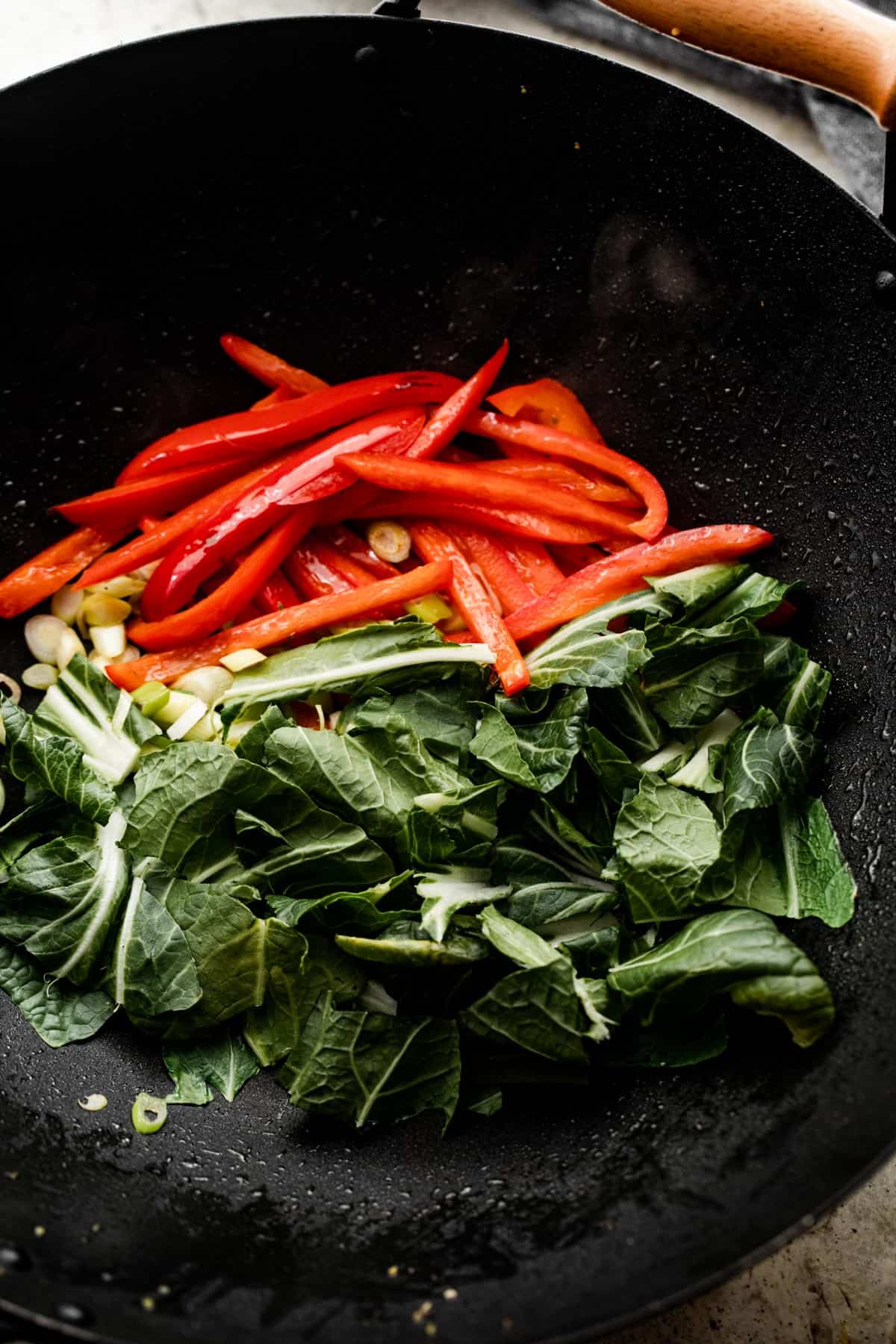 cooking chopped bok choy and thinly sliced red peppers in a black wok.