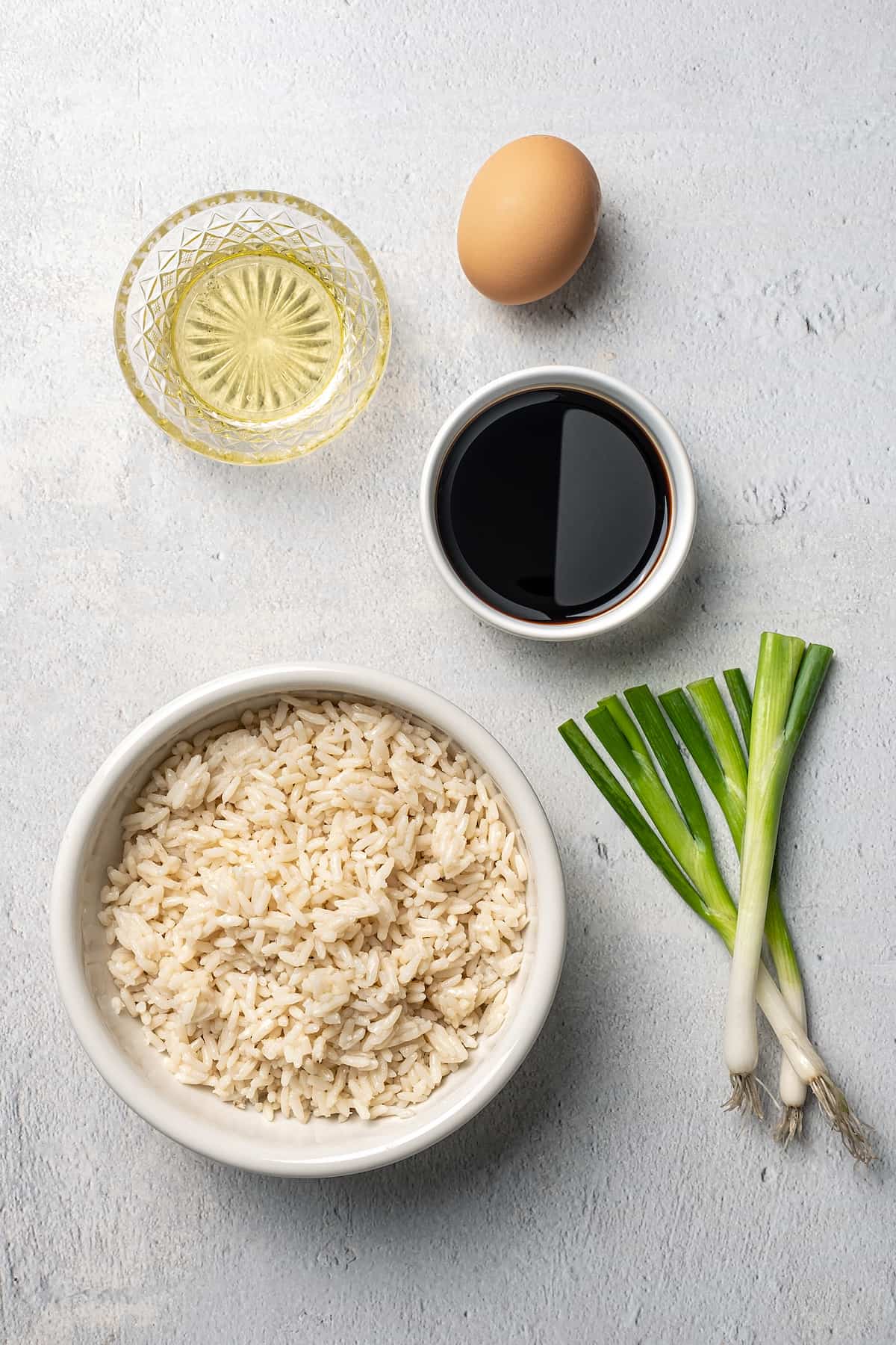 Bowls with rice, vinegar and soy sauce next to scallions and an egg